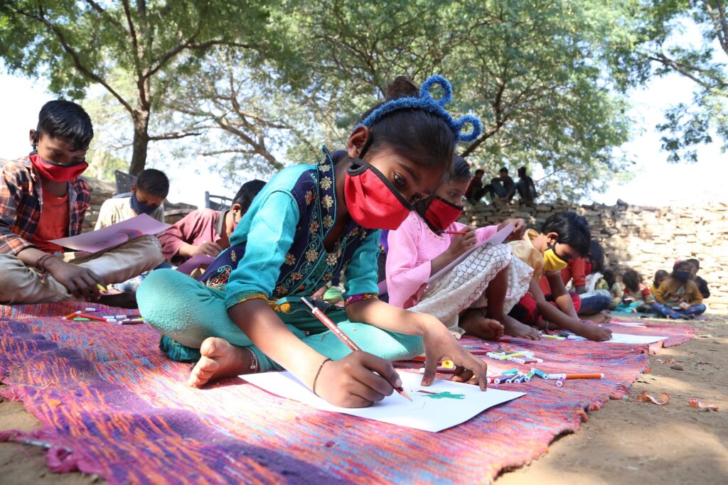 A class of young children sitting on the ground in open air class, wearing masks because of Covid virus, Rajasthan, India, 