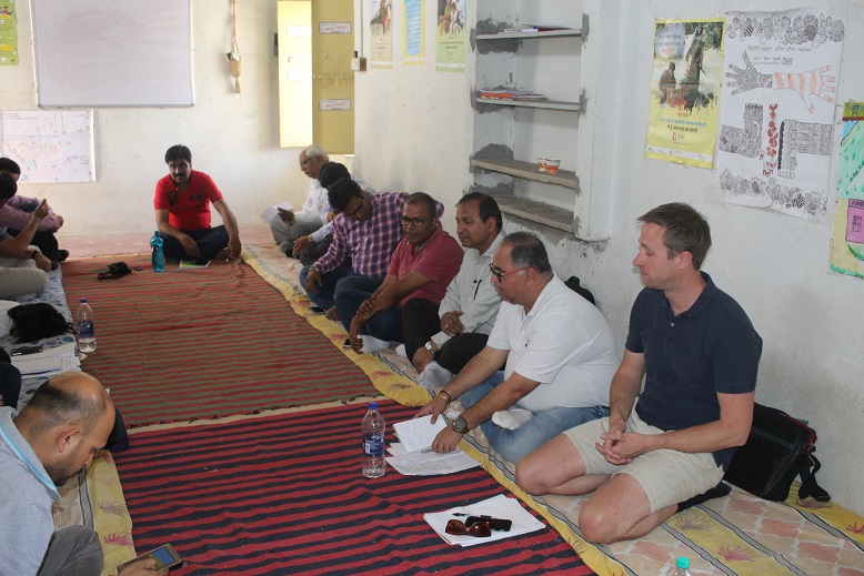 No Child Left Behind meeting in Budhpura. Men sitting on floor around edge of room.